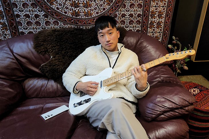 Music Artist Taebz sitting on a couch holding a guitar looking at the camera.